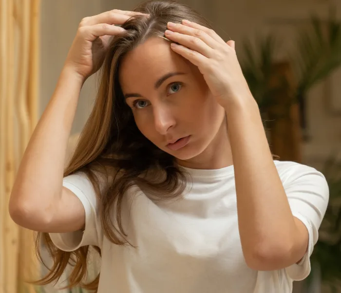 A woman pulling back her hair to examine a receding hairline